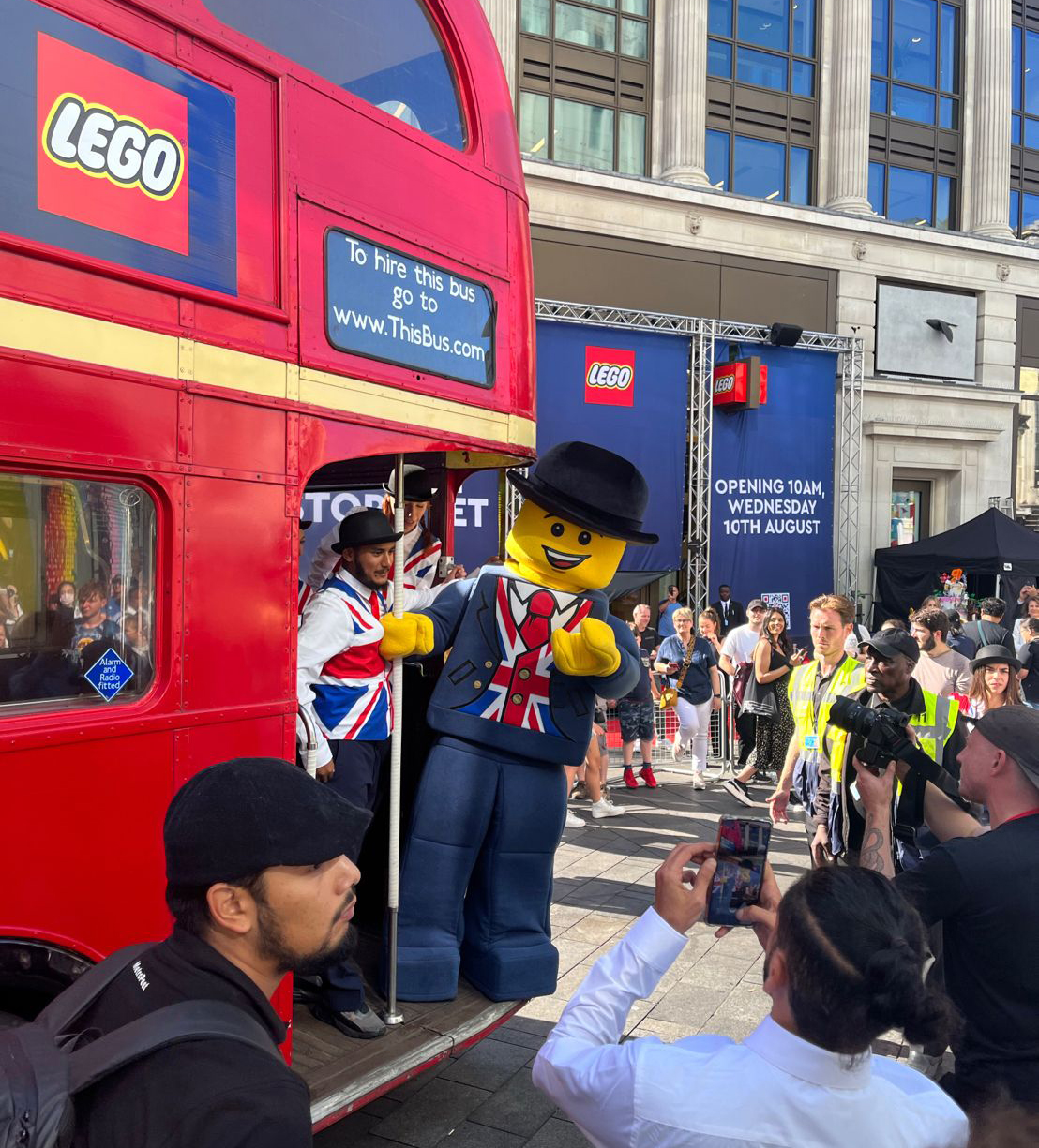 A lego man waves to the crowd from a bus